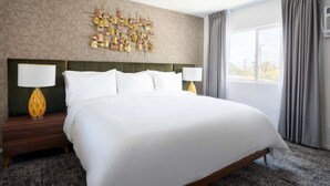 A hotel room with a large bed, two bedside tables with lamps, a geometric patterned wall, and a window with curtains. - Oasis In The California Desert | Pool. Adults Only (Palm Springs)