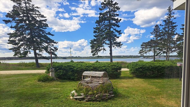 A grassy outdoor area with a bench, a birdhouse, and a view of a lake and trees. - Bright, Spacious Beachwalk Cottage: Ocean view, 5 minutes to sandy beaches (Sable River)