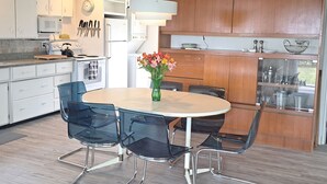 A modern kitchen with white cabinets, a microwave, a stove, and a dining area with a round table and chairs. - Bright, Spacious Beachwalk Cottage: Ocean view, 5 minutes to sandy beaches (Sable River)