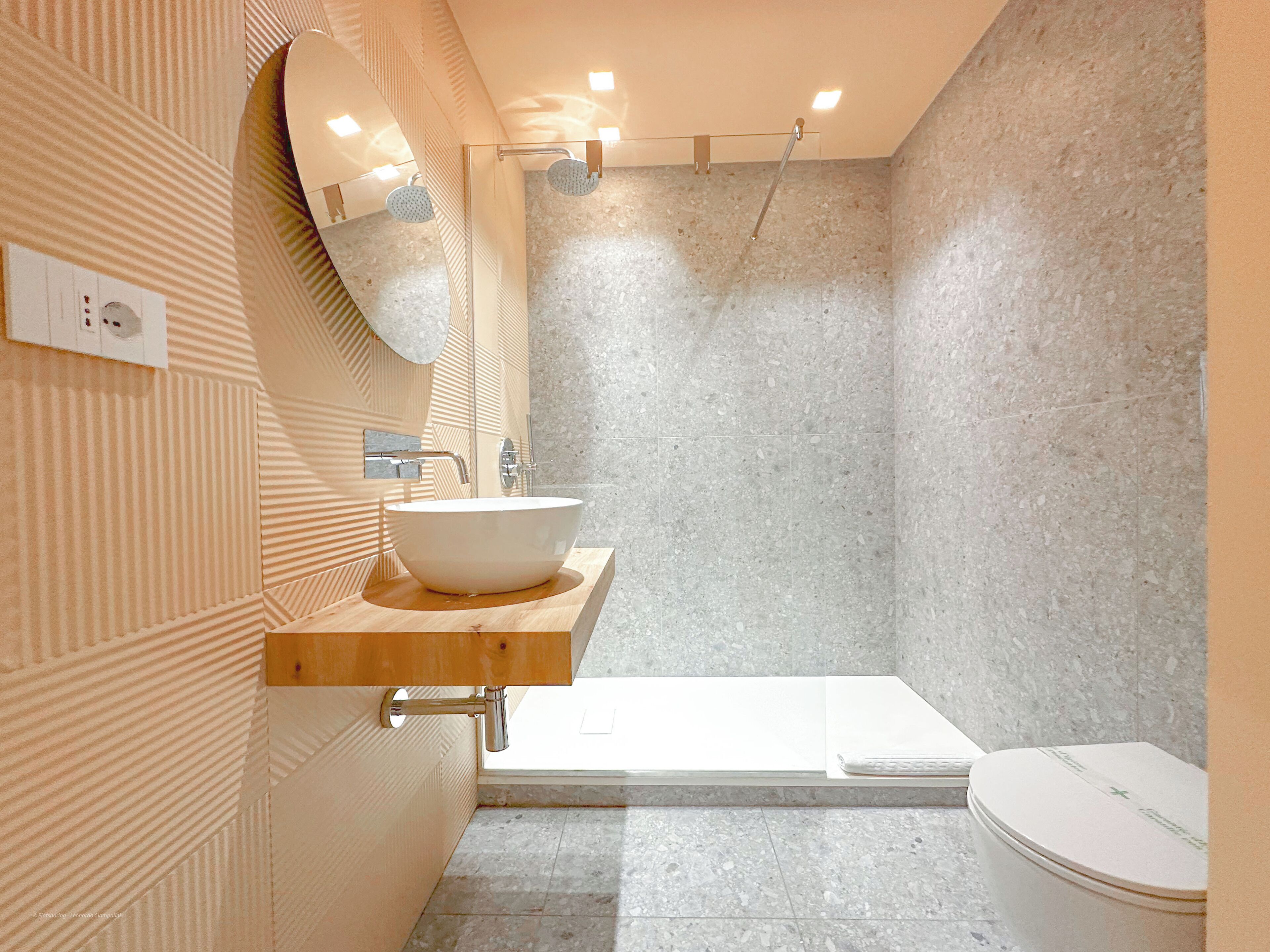 A modern bathroom with a large white sink, a shower, and a toilet.