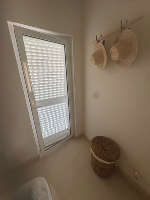 Une pièce avec un plafond en pente, une fenêtre avec des stores, un panier en osier et un porte-chapeaux fixé au mur.