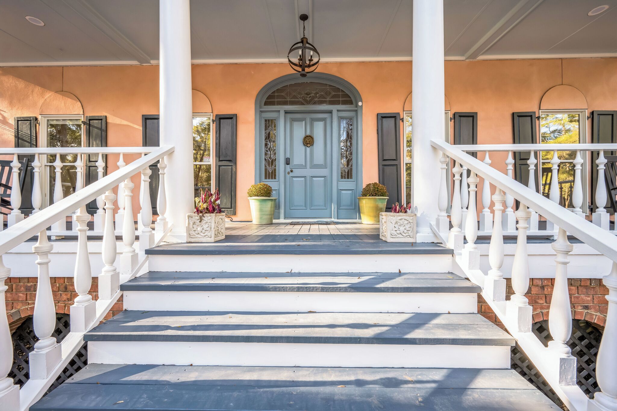 A porch with white railings and a blue door, leading to a brick wall.