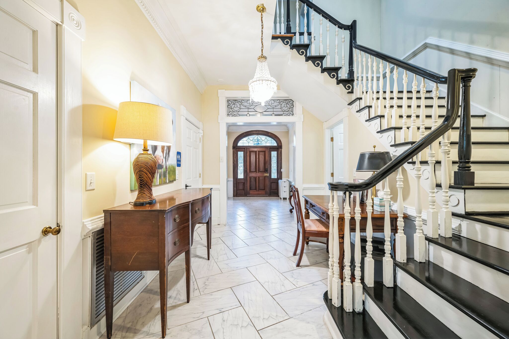 A grand hallway with a staircase, a chandelier, and a dining area with a table and chairs.