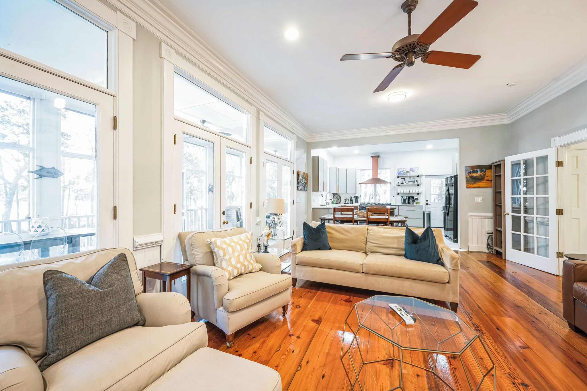A spacious living room with a wooden floor, a ceiling fan, and large windows.