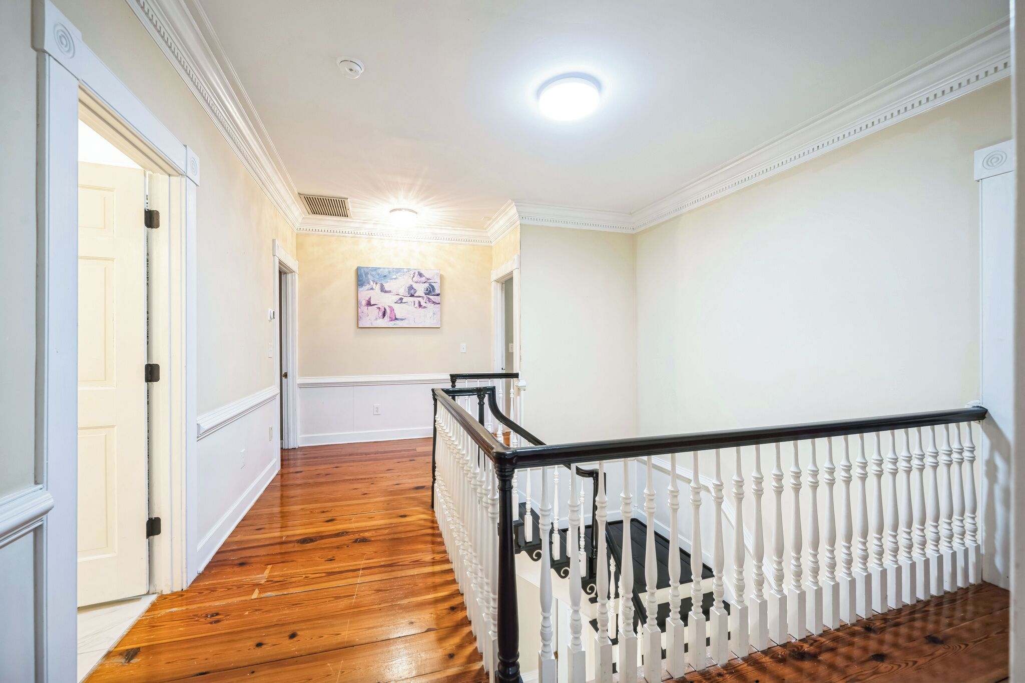 A hallway with wooden flooring, white walls, and a white railing with black balusters.