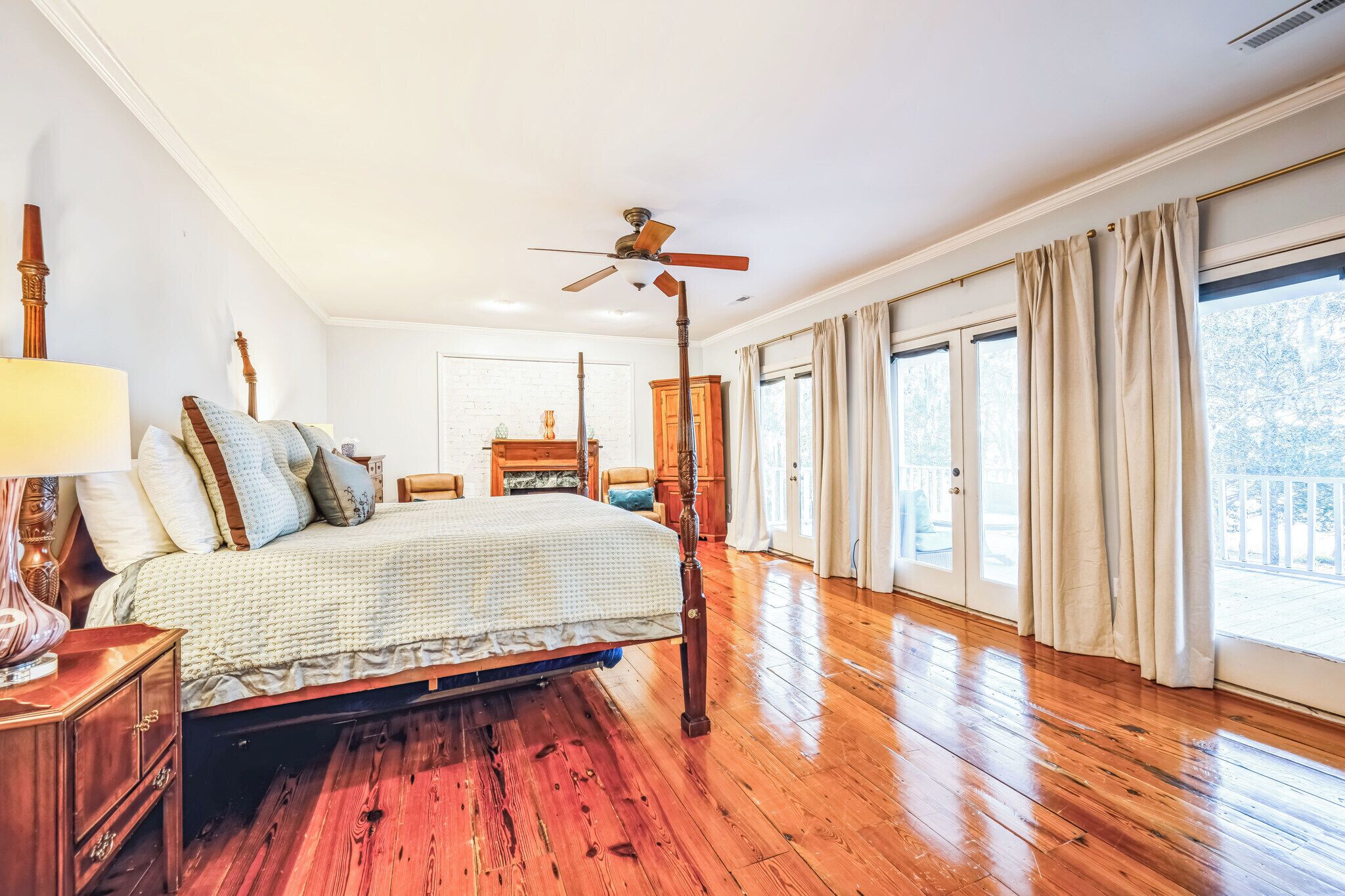 Ein geräumiges Schlafzimmer mit Holzboden, einem großen Himmelsbett, einem Deckenventilator und Blick ins Freie durch große Fenster.