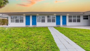 A modern building with a flat roof, a paved walkway, and a grassy area in front. - Charming Beachside Studio: King Bed, AC & Full Kitchen (Fort Lauderdale)