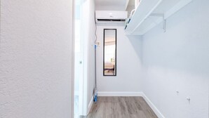 A narrow hallway with a wooden floor, white walls, and a mounted air conditioning unit. - Charming Beachside Studio: King Bed, AC & Full Kitchen (Fort Lauderdale)