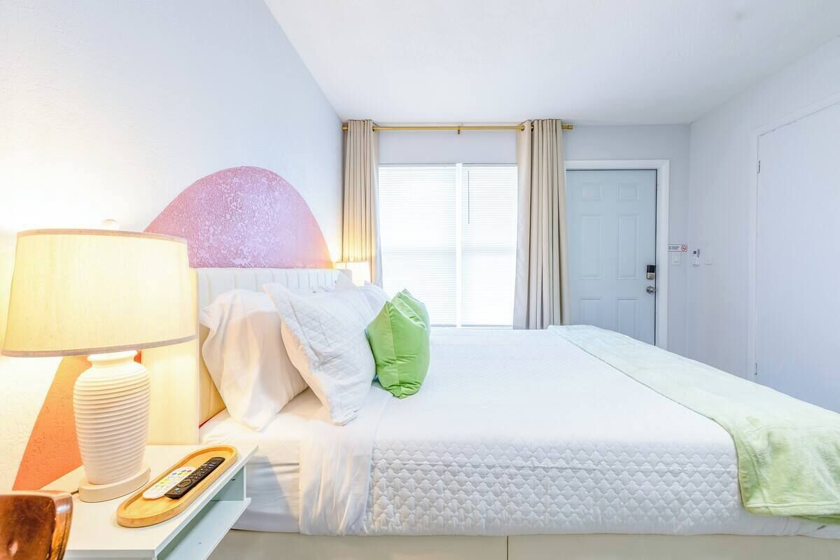 A hotel room with a bed, a bedside table with a lamp, a remote control, and a wall-mounted light fixture.