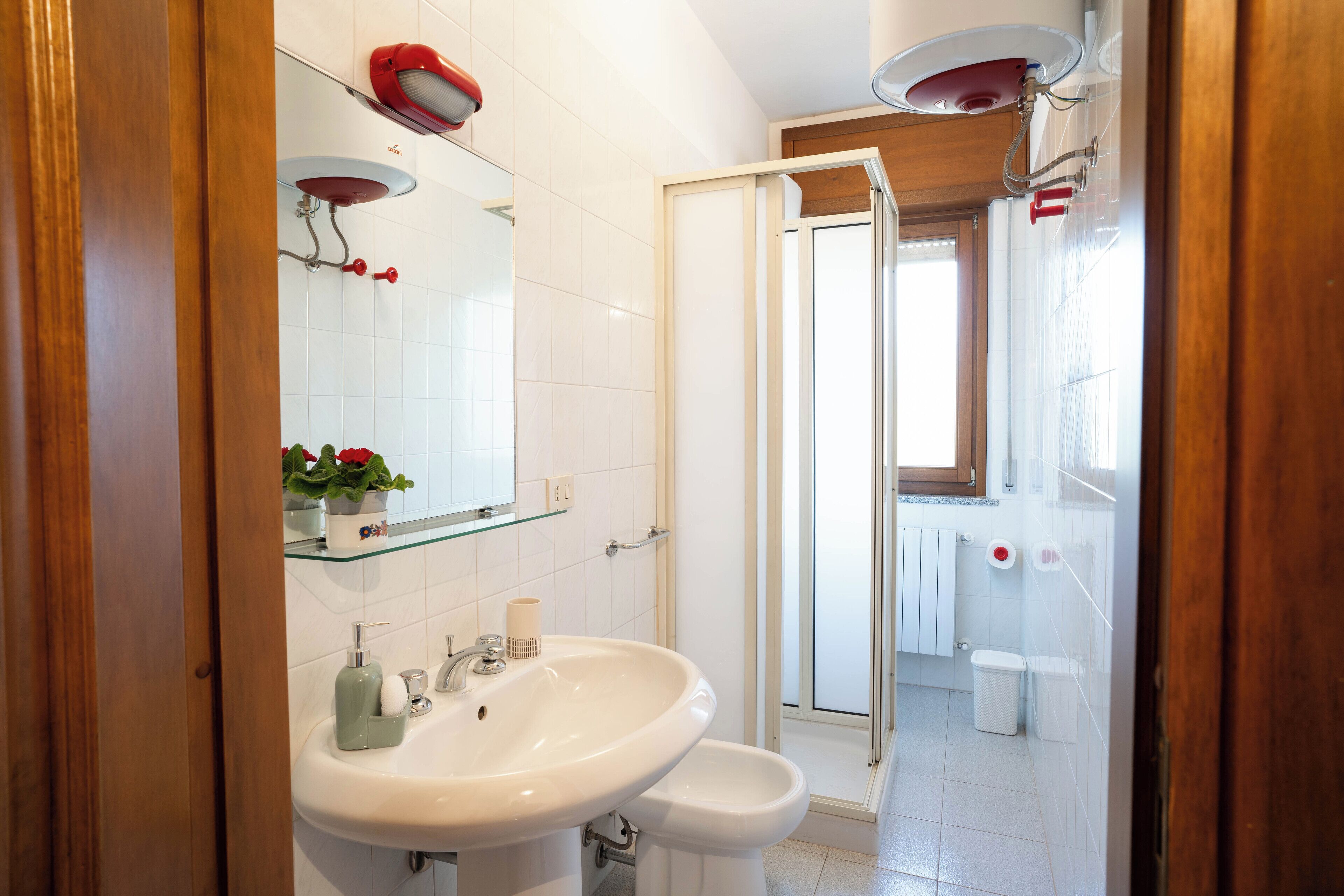 Un baño con lavamanos blanco, espejo, cabina de ducha de vidrio y retrete.