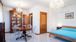 Un dormitorio con una cama de madera, una araña, una mesa de comedor con sillas y una estantería.