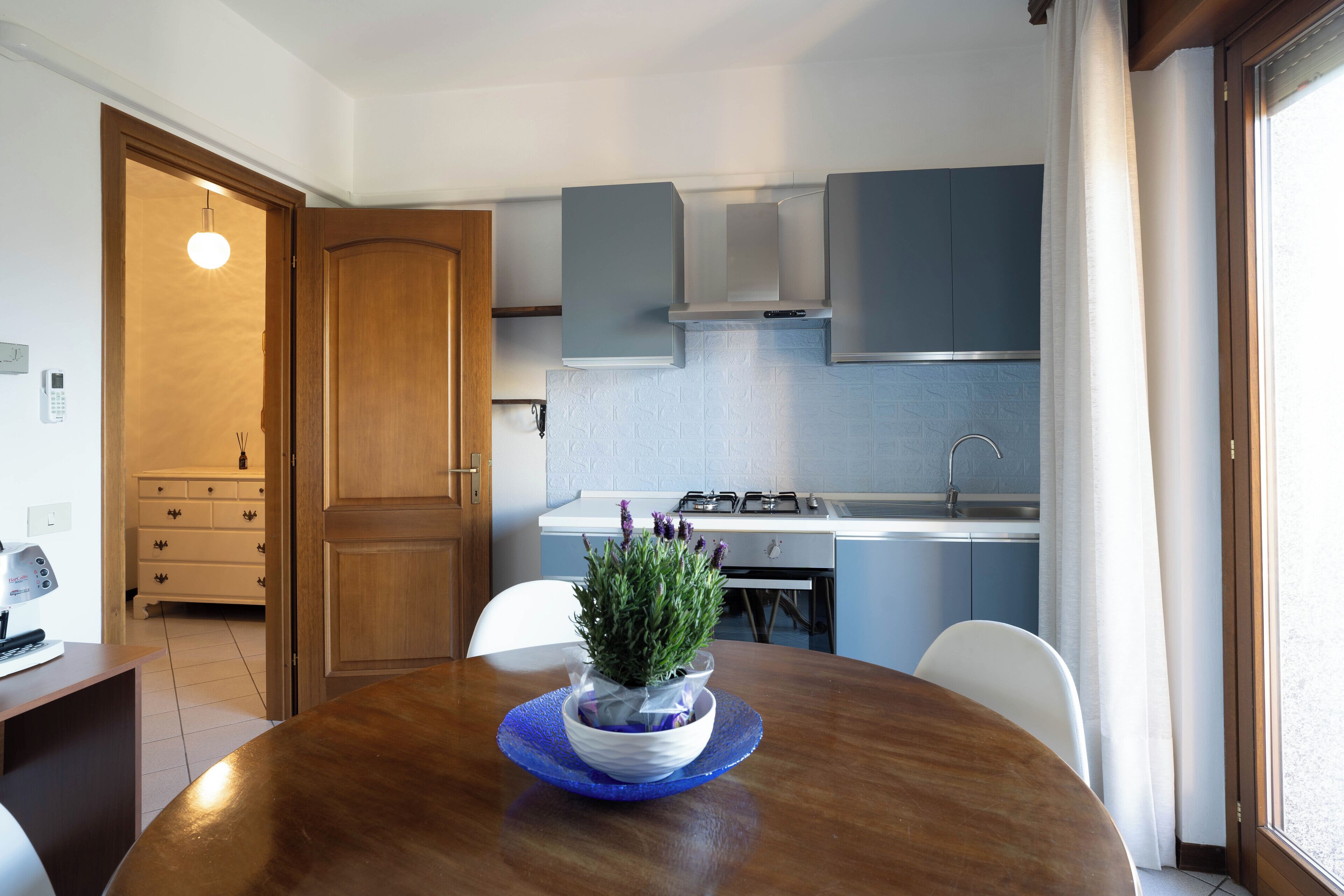 Una cocina compacta con área de comedor, que incluye una mesa de madera, una planta en maceta y un plato de vidrio azul.