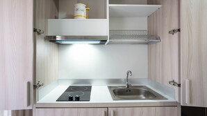 A compact kitchen with a built-in stove, sink, and upper shelf with a canister. - Casa Wanda Appartamento il Mirto (Oristano)