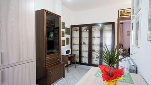 A room with a wooden cabinet, a microwave, a dining table with a vase, and a cabinet with glass doors. - Casa Wanda Appartamento il Mirto (Oristano)