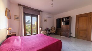 A hotel room with a large bed, a desk with a lamp, a chair, a small table with flowers, a bookshelf, and a wardrobe. - Casa Wanda Appartamento il Mirto (Oristano)