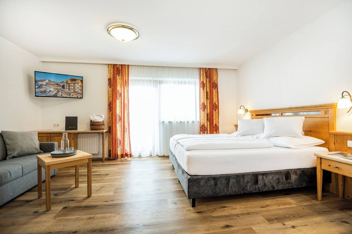 A hotel room with a bed, a desk, a chair, and a television on the wall.