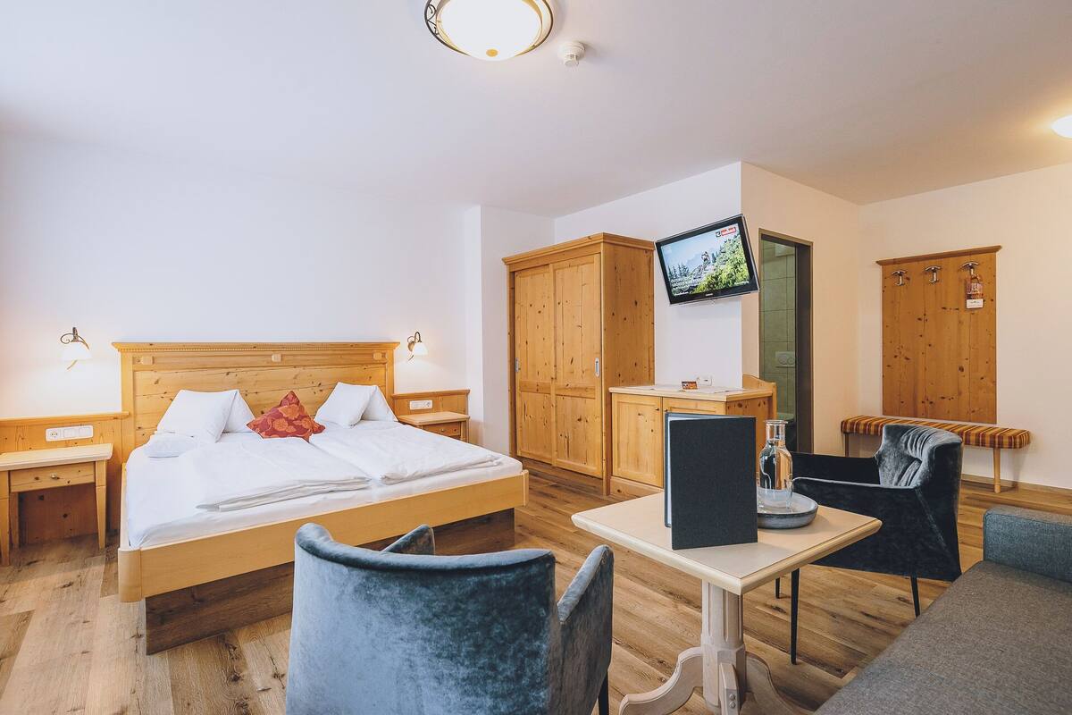 A hotel room with a bed, wooden wardrobe, TV, desk, chair, and a small table.