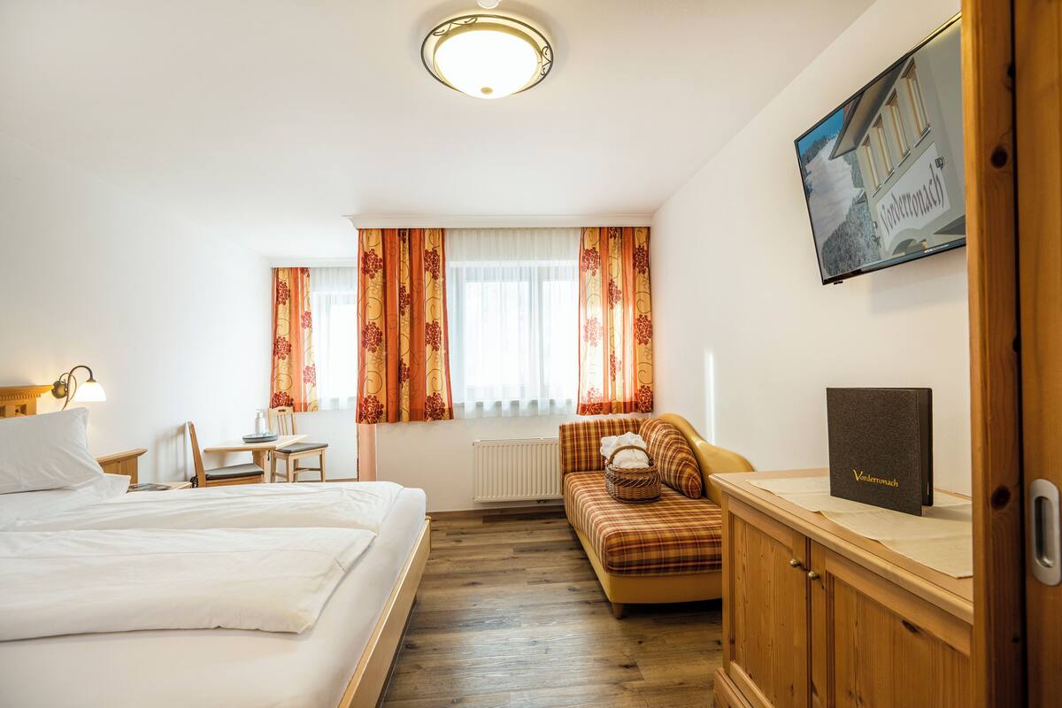 A hotel room with a bed, a sofa, a wooden cabinet, a television, and a window with curtains.