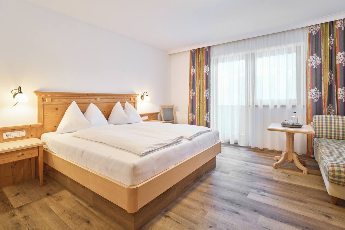A hotel room with a wooden bed, a wooden desk, a small table, and a sofa.