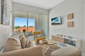 A modern living room with a sofa, a yellow armchair, a TV mounted on the wall, and a sliding glass door leading to an outdoor area. - Elegant 2BR Condo with Pool Access in Noord, Aruba (Noord)