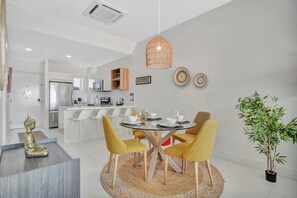 A modern dining area with a round table, yellow chairs, and a hanging light fixture. - Elegant 2BR Condo with Pool Access in Noord, Aruba (Noord)
