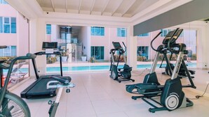 Een fitnessruimte met loopbanden, elliptische trainers en een zwembad op de achtergrond.