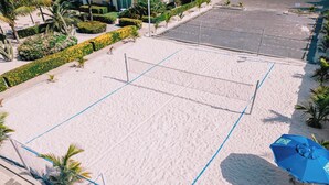 Een strandvolleybalveld met een net, omringd door zand en palmbomen.