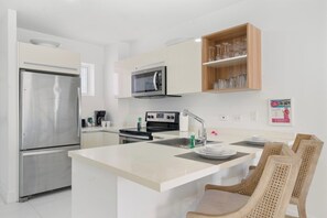 A modern kitchen with stainless steel appliances, a central island, and wooden chairs.