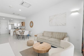 Un salon moderne avec un canapé beige, une table basse ronde et un coin repas avec des chaises.
