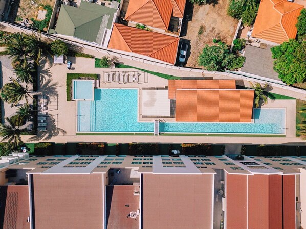 An aerial view of a hotel with a swimming pool, parking area, and multiple buildings with red roofs.