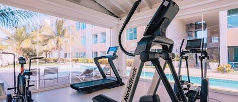 A gym with treadmills and stationary bikes, large windows, and a pool view.