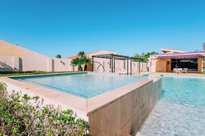 A swimming pool with a sunshade structure, surrounded by a low wall and greenery. - Modern Caribbean 2BR Condo with Pool Access, Noord (Noord)