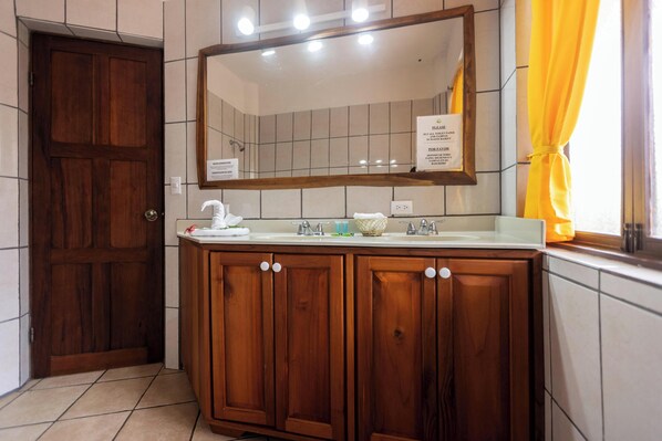 A bathroom with a wooden vanity, a large mirror, and a sign instructing to please not flush paper towels.