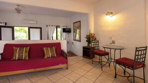 Ein Wohnzimmer mit einem roten Sofa, zwei Sesseln, einem kleinen Tisch, einem Deckenventilator, einem Fernseher und einer Wandleuchte.