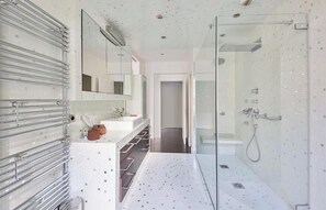 Une salle de bain moderne avec une douche à parois de verre, un lavabo blanc avec un miroir et des porte-serviettes chromés.