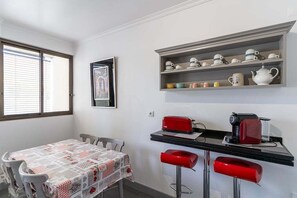 A compact kitchen with a table set for four, a coffee machine, and a shelf with various kitchenware. - GuestReady - Beautiful sea view in Funchal (Funchal)
