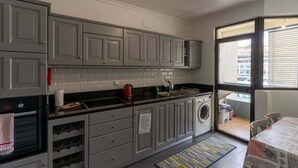 Una cocina compacta con armarios grises, encimera negra, horno integrado y lavadora.