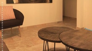 Une pièce dans laquelle on trouve un grand tableau abstrait accroché au mur, une chaise noire avec un coussin rose et une petite table ronde.