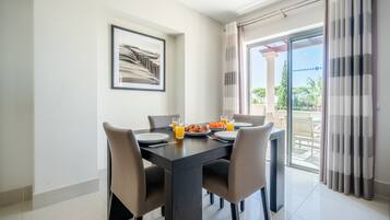 A dining area with a table set for two, a framed picture on the wall, and a view of the outdoors through a glass door.