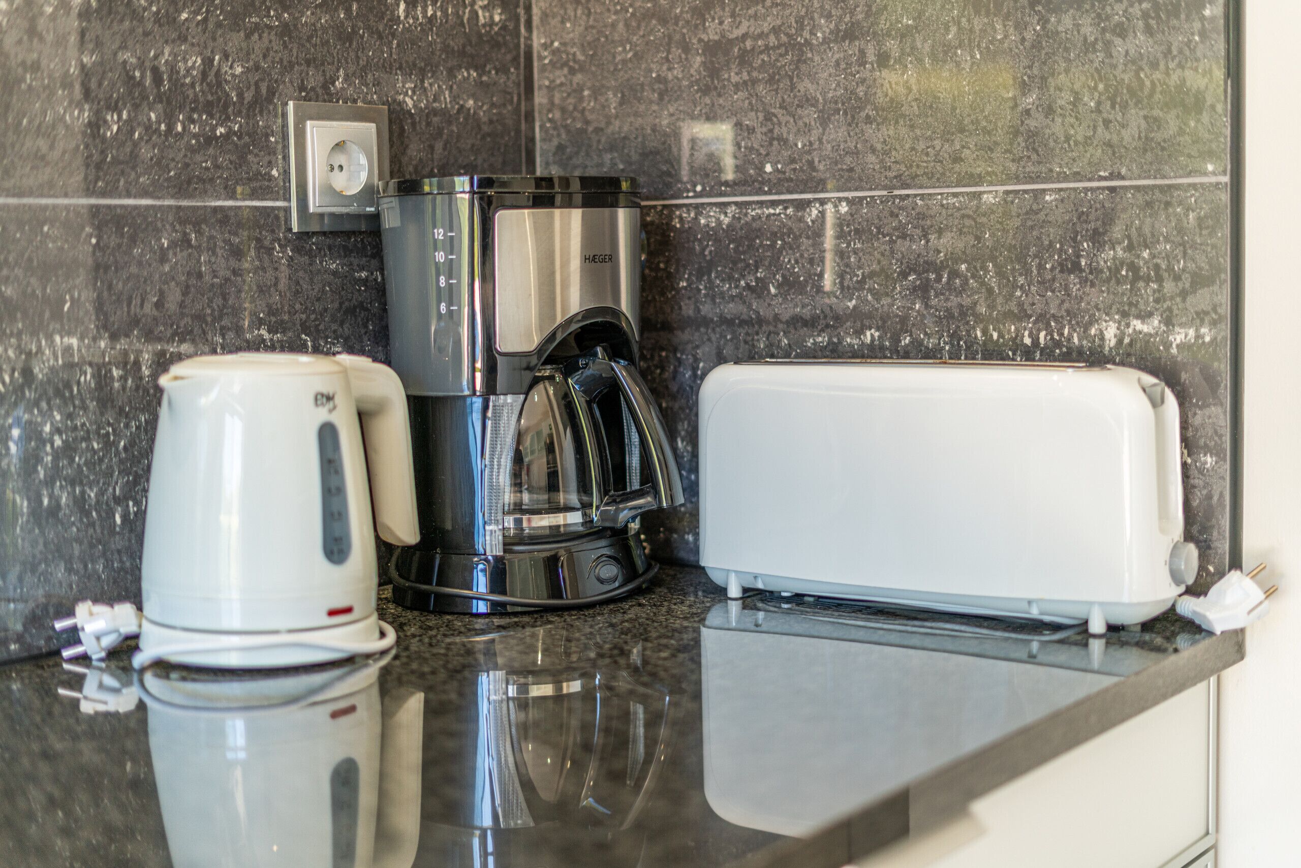 A kitchen with a coffee maker, toaster, and a wall socket.