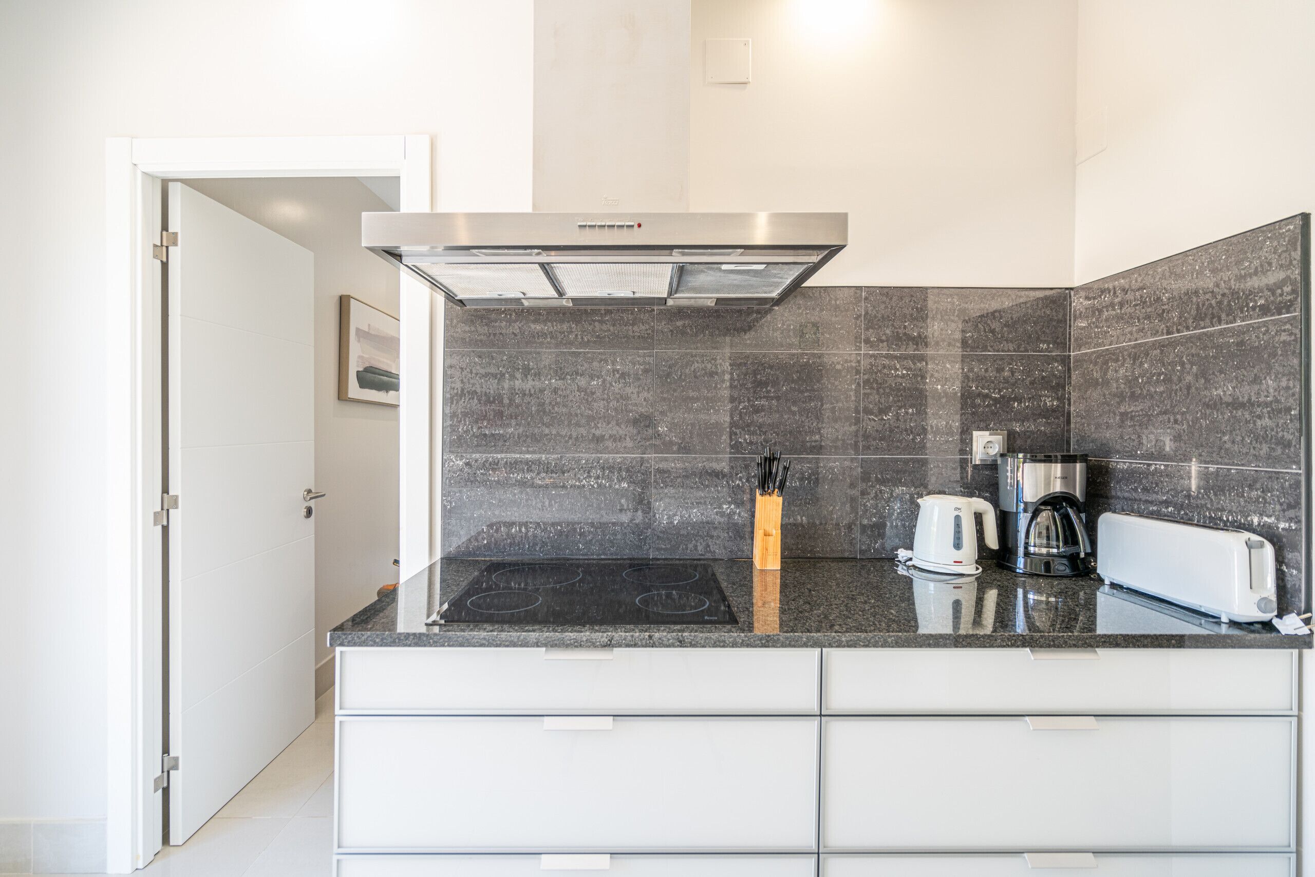 A modern kitchen with a stainless steel range hood, a built-in stovetop, a coffee maker, and a toaster.