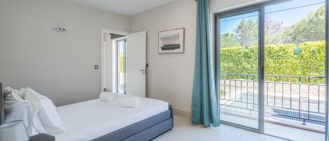 Ein modernes Schlafzimmer mit Bett, Schreibtisch und Balkon mit Blick auf Grünflächen.