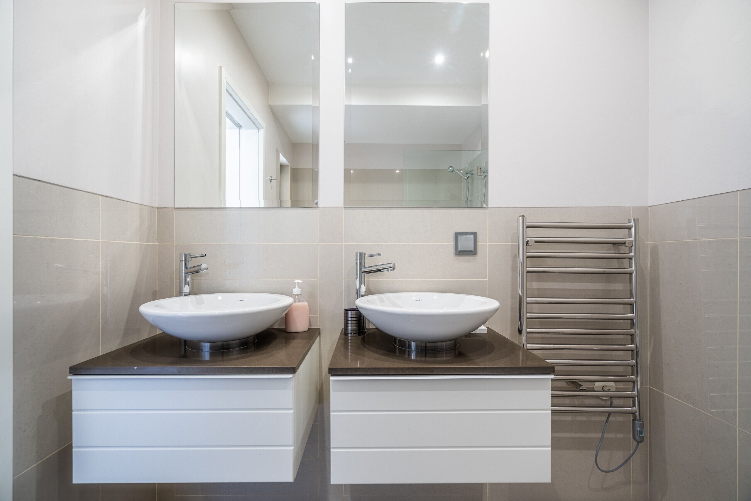 Un baño moderno con dos lavamanos, un espejo y un perchero para toallas.