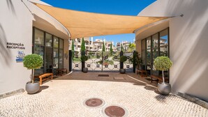 Ένας χώρος υποδοχής με πλακάκια στο δάπεδο, γλάστρες με φυτά και ένα ξύλινο παγκάκι.