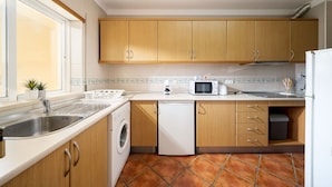 A compact kitchen with wooden cabinets, a built-in washing machine, a microwave, and a sink. - Albufeira Palm Tree With Pool by Homing (Albufeira)
