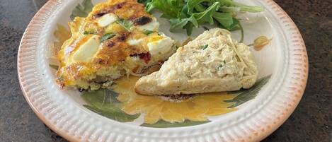 Un plato con una porción de quiche, un trozo de pastel y una ensalada acompañante sobre un plato de cerámica.