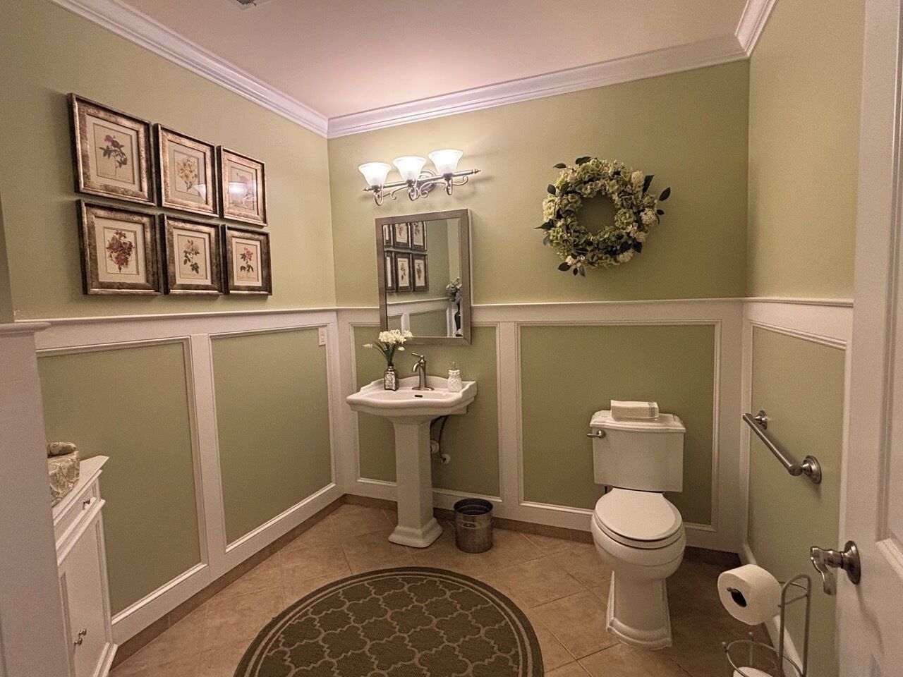 A bathroom with a pedestal sink, toilet, and a decorative wreath on the wall.