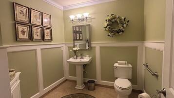 A bathroom with a pedestal sink, toilet, and a decorative wreath on the wall.