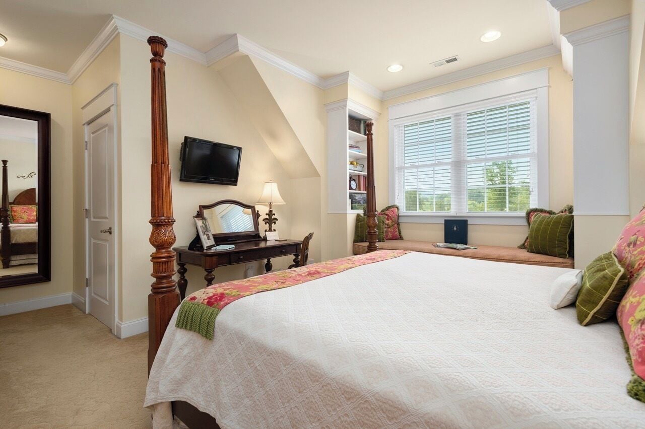A bedroom with a four-poster bed, a television mounted on the wall, and a window with blinds.