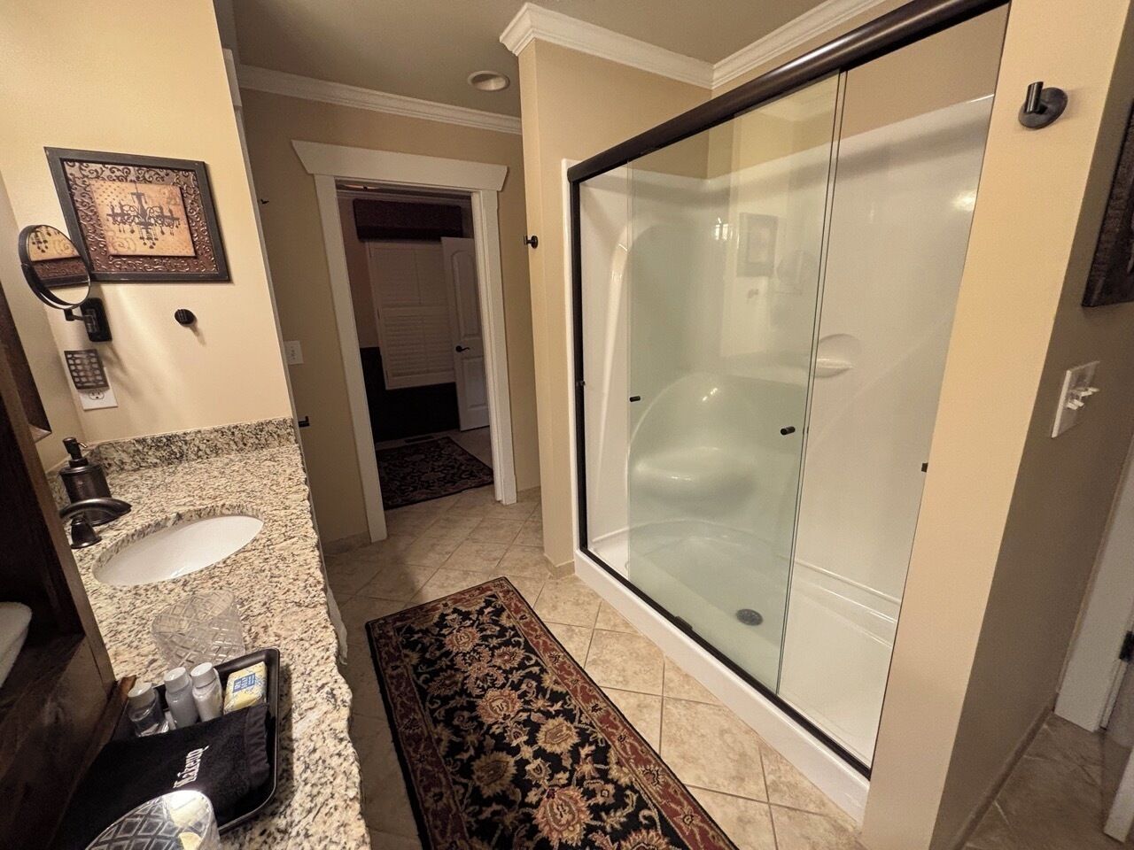 A bathroom with a glass-enclosed shower, a sink with a granite countertop, and a patterned rug on the floor.